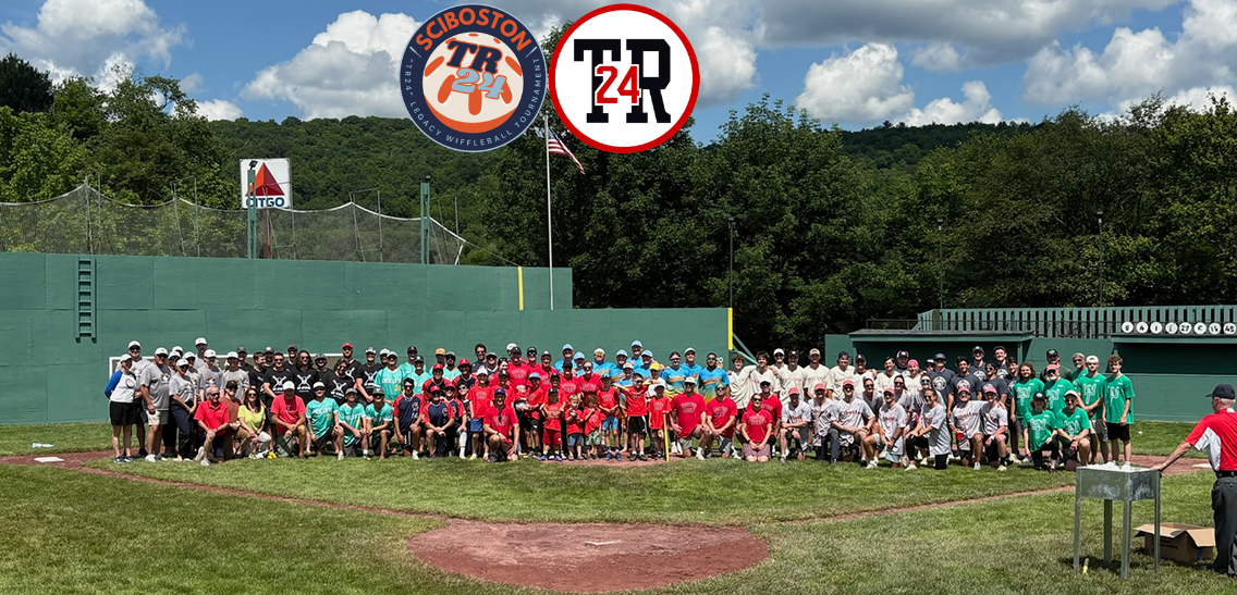 ID: a horizontal image of all of the volunteers and players at the with a ball tournament. The group is at little Fenway with trees in the background. Event logos are at the top center.