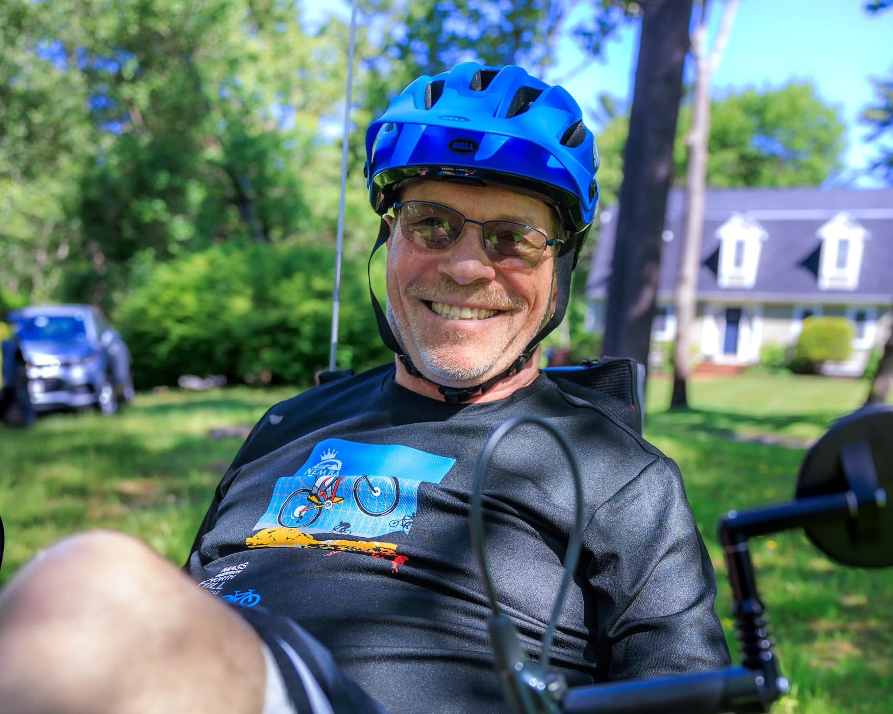 ID: Ed outside wearing a helmet sitting on his adapted bicycle