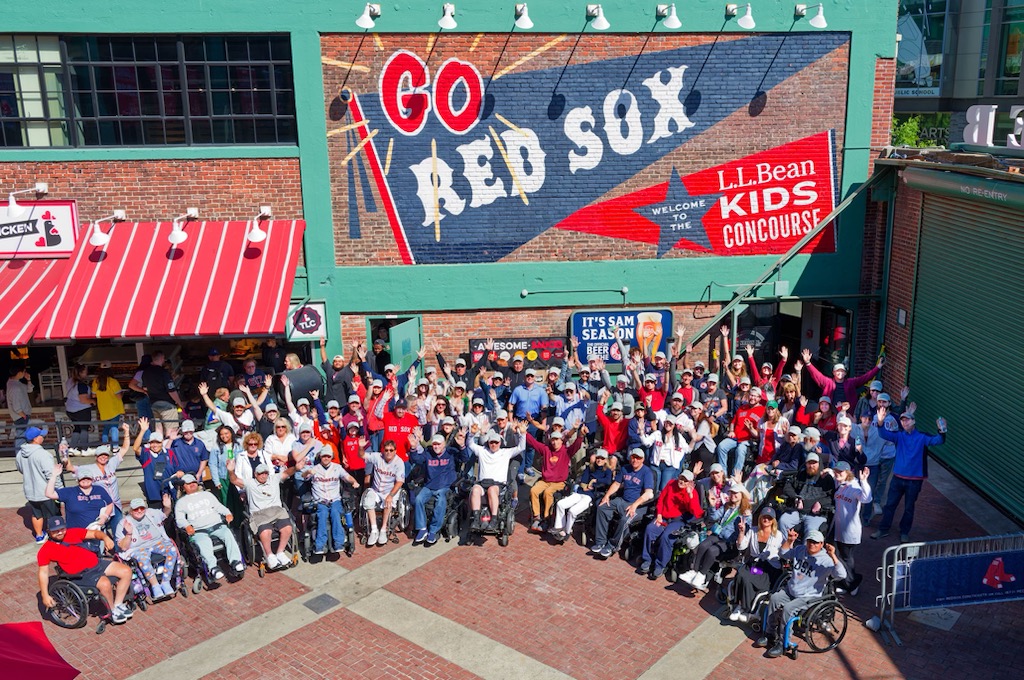 Image ID: a group of wheelchair users and non-wheelchair users gathered in front of a large brick wall with go Red Sox painted on