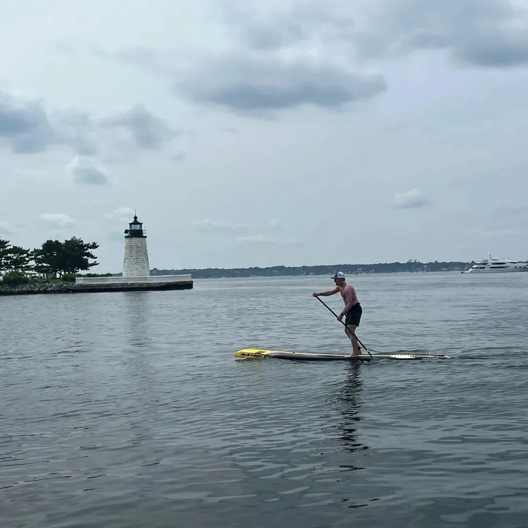 Image description: Allie paddle boarding on open water with a lighthouse in the background.